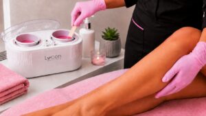 Professional esthetician preparing pink wax in a LYCON wax heater before a leg waxing treatment.